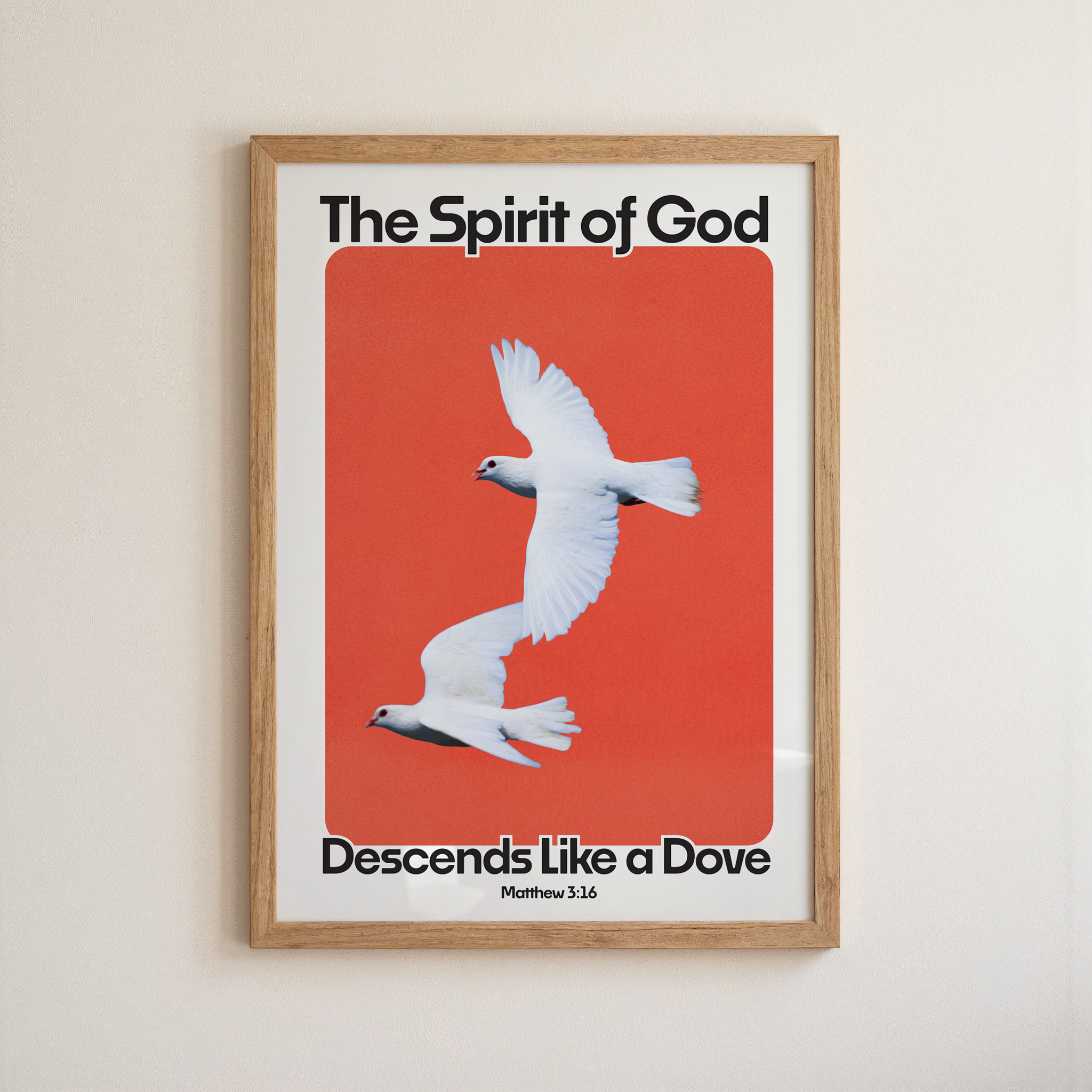 A framed art print featuring two white doves flying against a solid red-orange background, with the text 'The Spirit of God' at the top and 'Descends Like a Dove' at the bottom, mounted on a light beige wall.